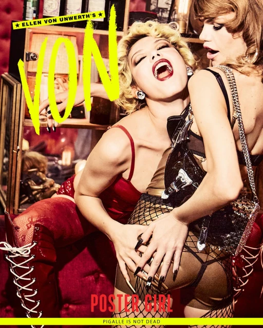 Two women pose together indoors for a magazine cover; one touches the other’s rear end as both pose in dark lighting.