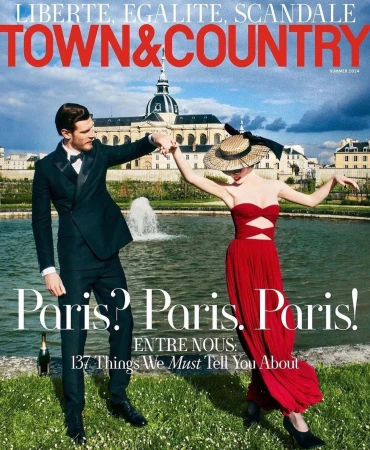 Magazine cover featuring a man in a suit and a woman in a red dress, holding hands in front of a building and a fountain in Paris.