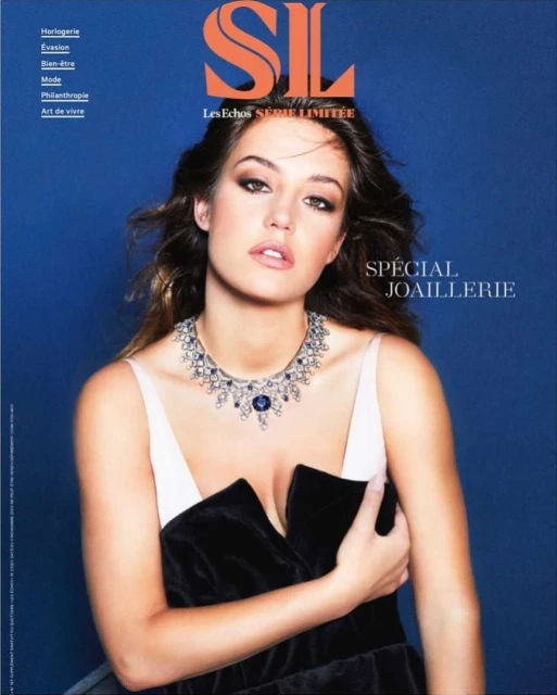 Magazine cover featuring a model wearing a statement necklace and black dress against a blue backdrop with bold magazine text.