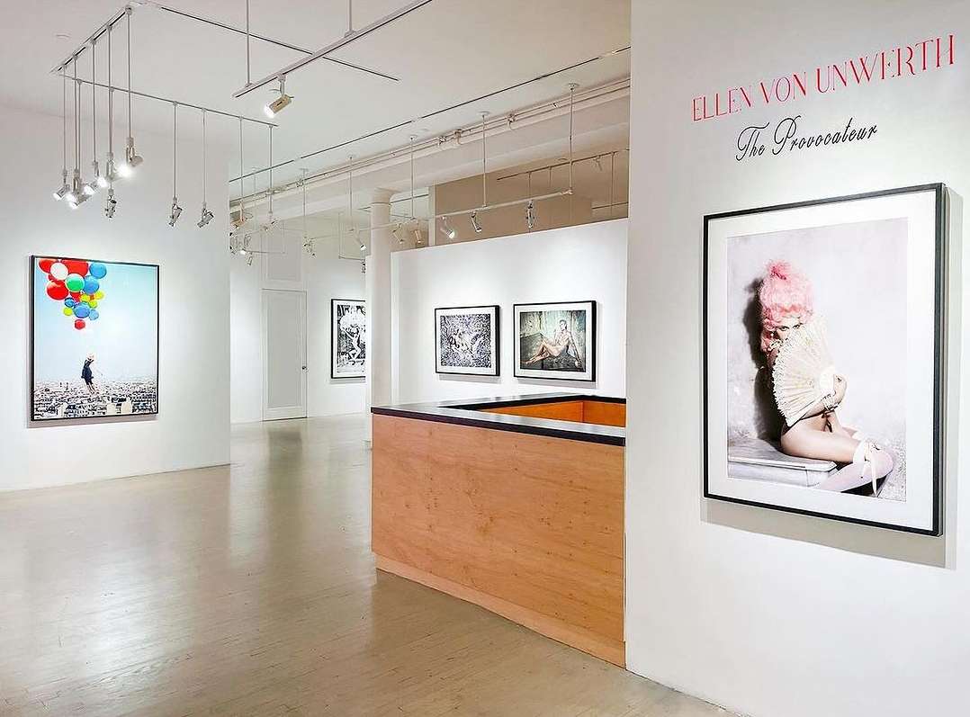 Gallery showcasing fine art photography, featuring a portrait with a model wearing a pink wig and holding a fan, alongside other framed artworks.
