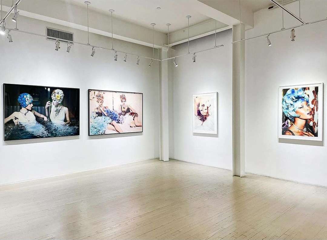 Art gallery interior showcasing framed portraits of women with elaborate headwear displayed on white walls with track lighting above.