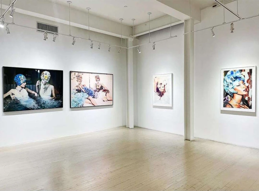 Art gallery interior showcasing framed portraits of women with elaborate headwear displayed on white walls with track lighting above.