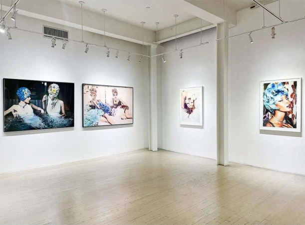 Art gallery interior showcasing framed portraits of women with elaborate headwear displayed on white walls with track lighting above.