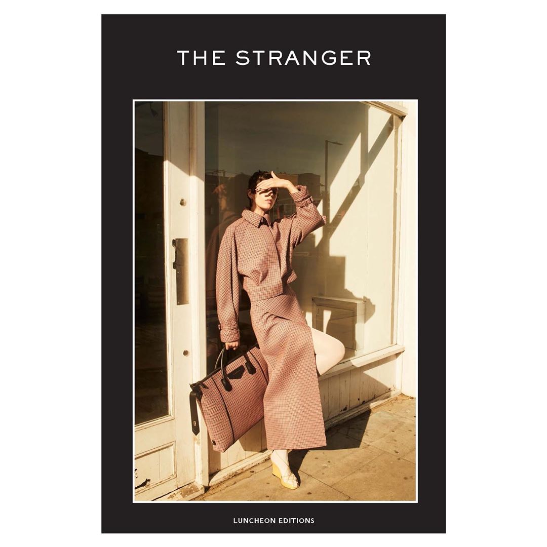 Fashion magazine cover featuring a woman in a patterned suit and sunglasses, holding a bag against a light, sunlit exterior.