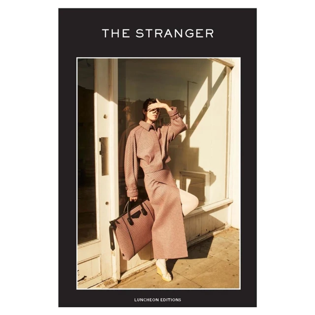 Fashion magazine cover featuring a woman in a patterned suit and sunglasses, holding a bag against a light, sunlit exterior.