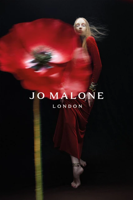 Jo Malone London campaign featuring an adult female in a red dress and bracelets, beside a blurred red flower against a black background.
