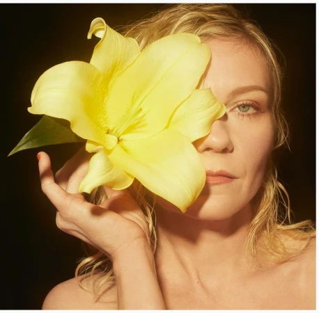 Kirsten Dunst holding a large yellow lily flower covering half her face in a portrait by Emma Summerton