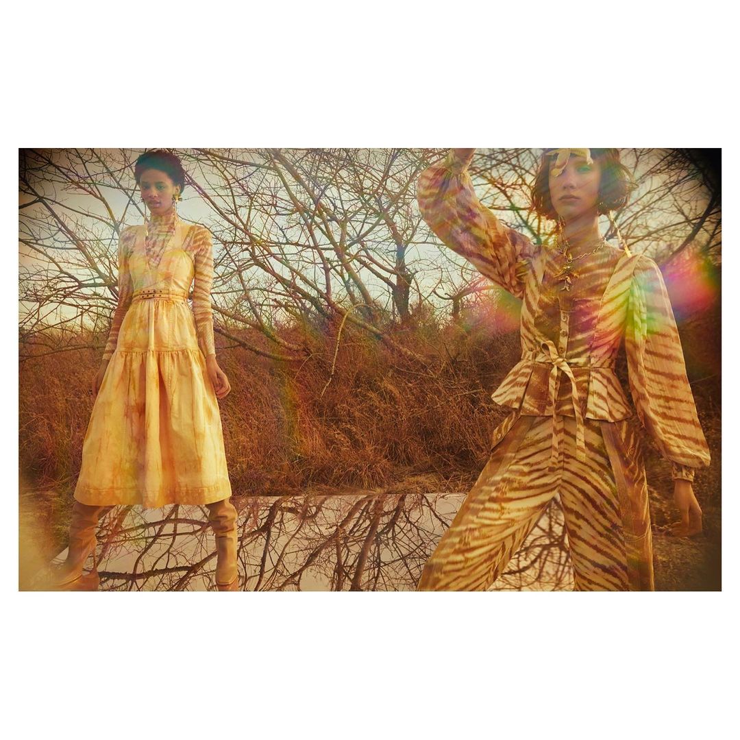 Two women in animal-print fashion pose outdoors near water, with bare trees in the background, creating a visually striking editorial image.