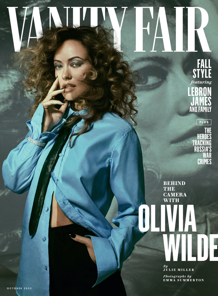 Olivia Wilde on Vanity Fair cover, October 2022. She wears an open light-blue blouse with curly hair, set against a blurred portrait.