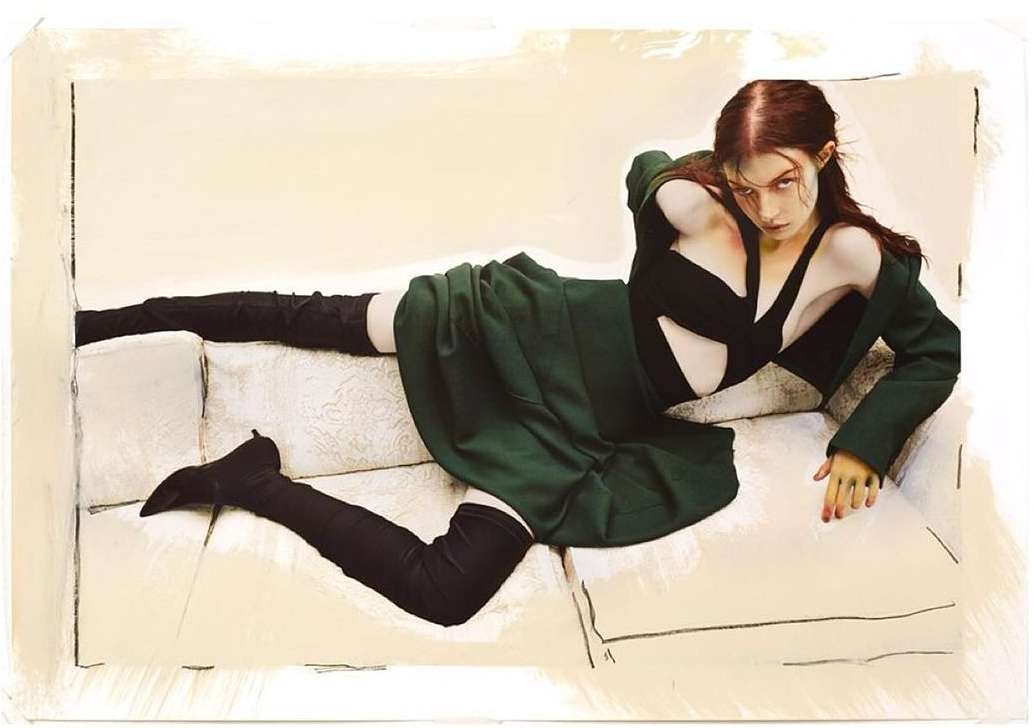 A woman in a black top, green skirt, and black boots reclines on a patterned off-white couch. The image appears to be a digital painting.