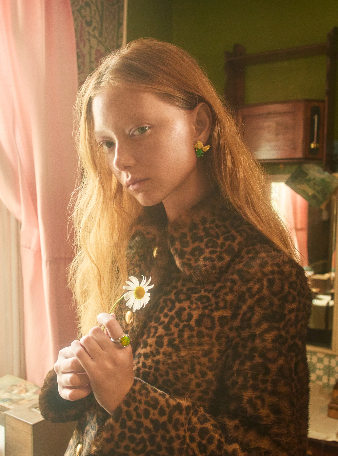 Portrait of a woman in a leopard-print coat holding a daisy flower indoors with soft, natural lighting and a vintage-inspired setting.
