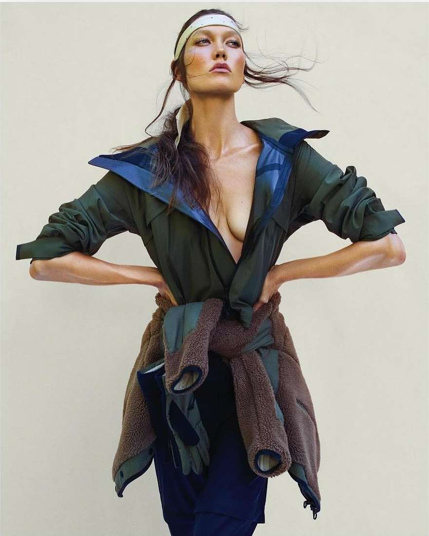 Karlie Kloss wearing a green jacket with a brown fleece tied around her waist and a headband against a light background
