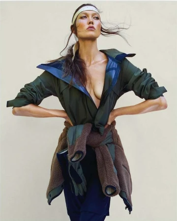 Karlie Kloss wearing a green jacket with a brown fleece tied around her waist and a headband against a light background