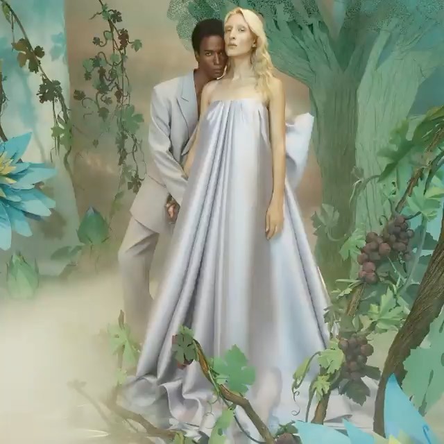 A fashion shot features an interacial couple, where a blonde woman in a silver dress is partially embraced by a man in a gray suit.