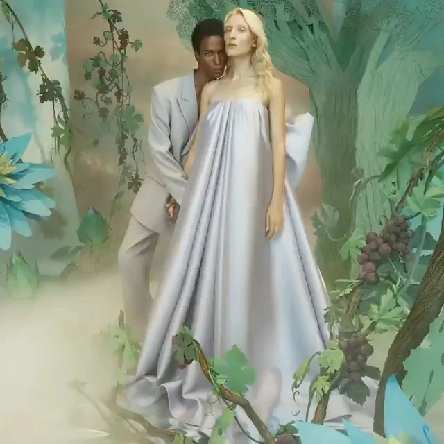 A fashion shot features an interacial couple, where a blonde woman in a silver dress is partially embraced by a man in a gray suit.