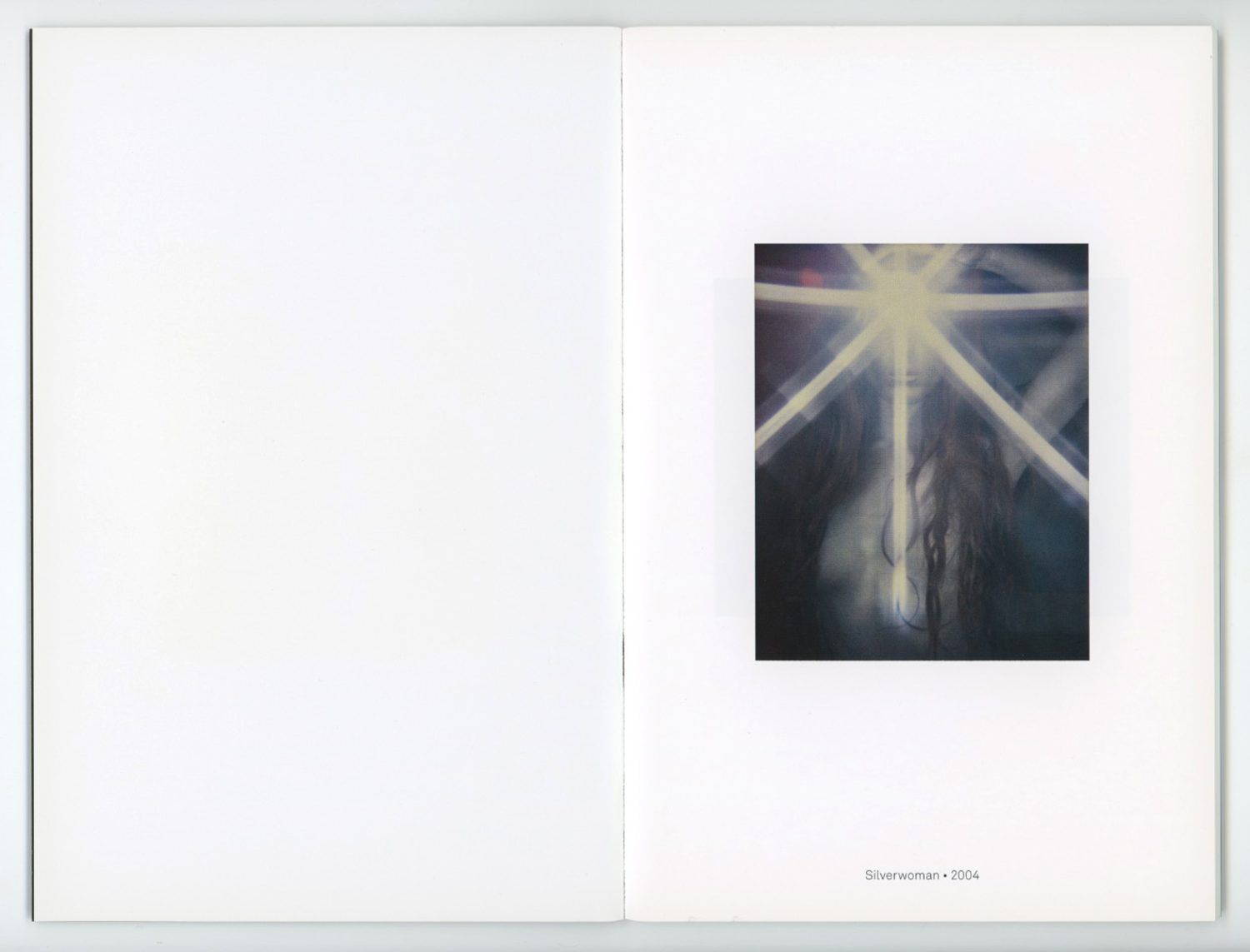 Blurred artful photograph of a woman's face with glowing light rays and dark flowing hair, mounted in an art book against a white background.