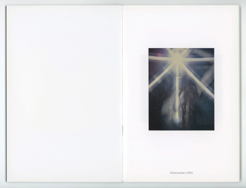 Blurred artful photograph of a woman's face with glowing light rays and dark flowing hair, mounted in an art book against a white background.