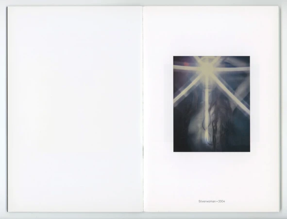Blurred artful photograph of a woman's face with glowing light rays and dark flowing hair, mounted in an art book against a white background.