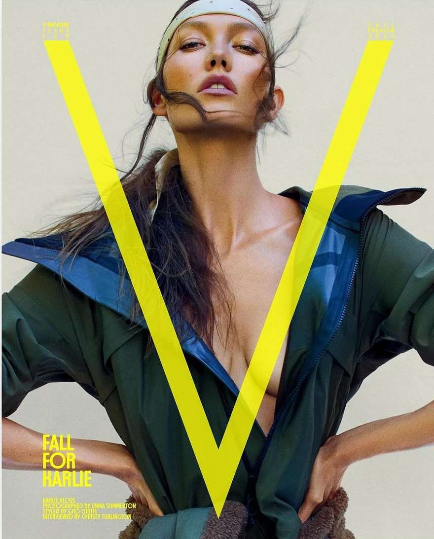 Close-up studio shot of adult female model in green jacket and tan headband posing behind yellow V logo on fashion magazine cover.