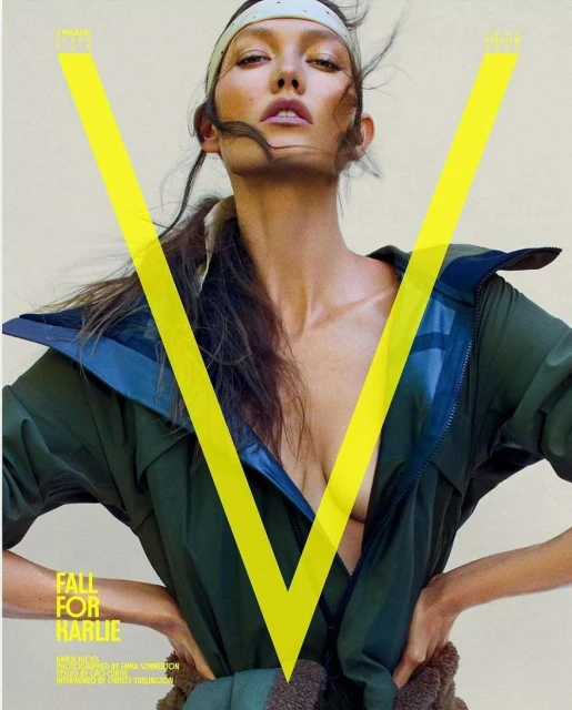 Close-up studio shot of adult female model in green jacket and tan headband posing behind yellow V logo on fashion magazine cover.
