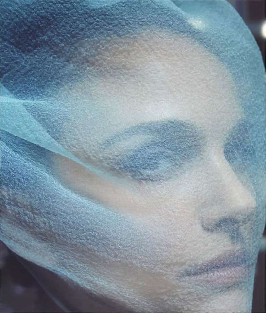 Adult female with cool skin tones looks off camera while wearing a translucent surgical cap in a studio with soft, diffused lighting.