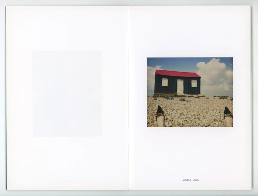 Architectural photo in a photography book shows a small building with a red roof on a rocky landscape under a cloudy sky.