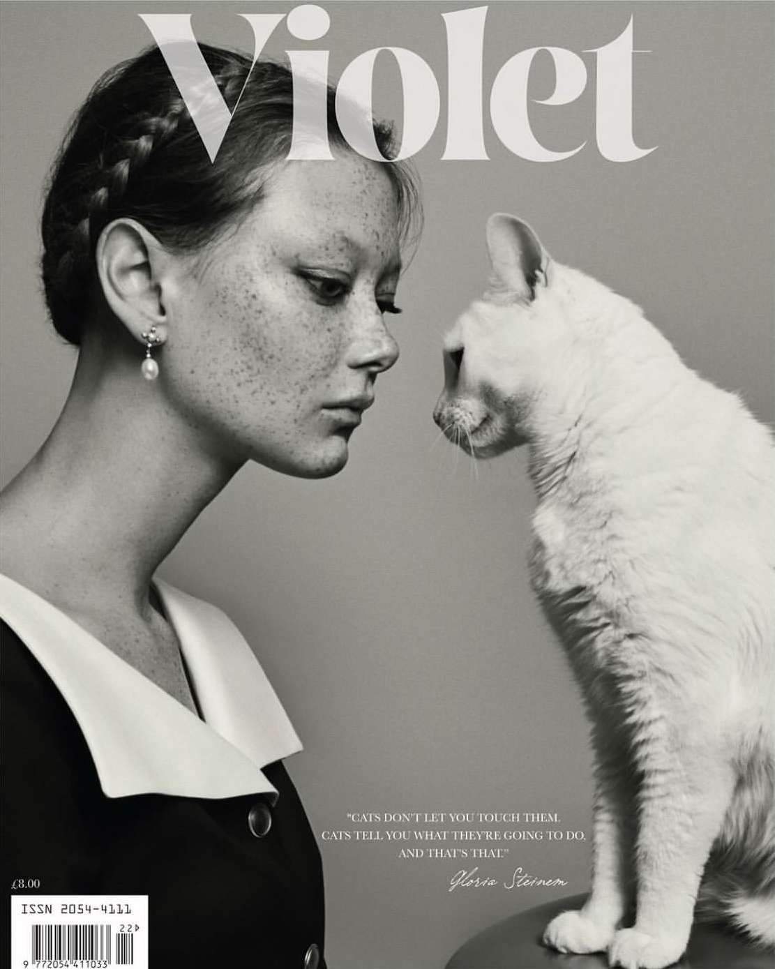 Magazine cover featuring a young woman with freckles looking at a white cat against a gray background in black and white.