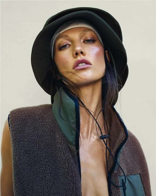 Close-up of a woman wearing a bucket hat and a fleece vest. The subject has medium skin, long brown hair, and neutral facial expression.
