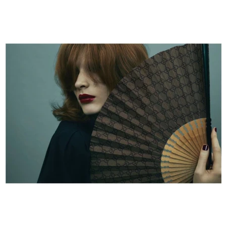 Woman with auburn hair and red lipstick holding a monogram patterned folding fan by Emma Summerton
