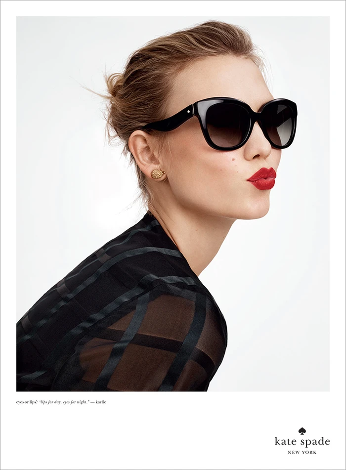 Profile view of a woman wearing oversized black sunglasses and red lipstick against a plain white studio background.