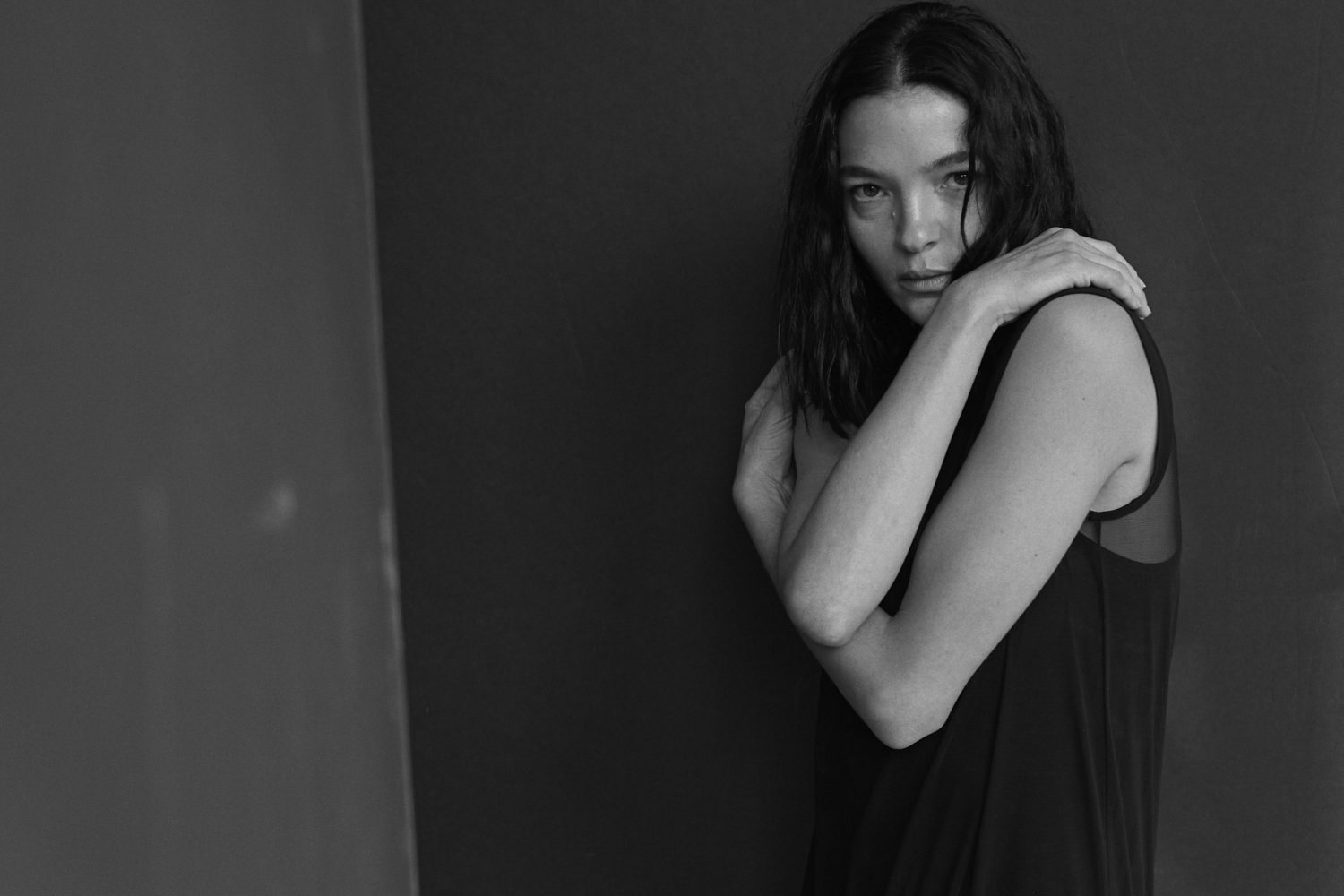 Black and white portrait of a woman with dark hair embracing herself against a dark textured background