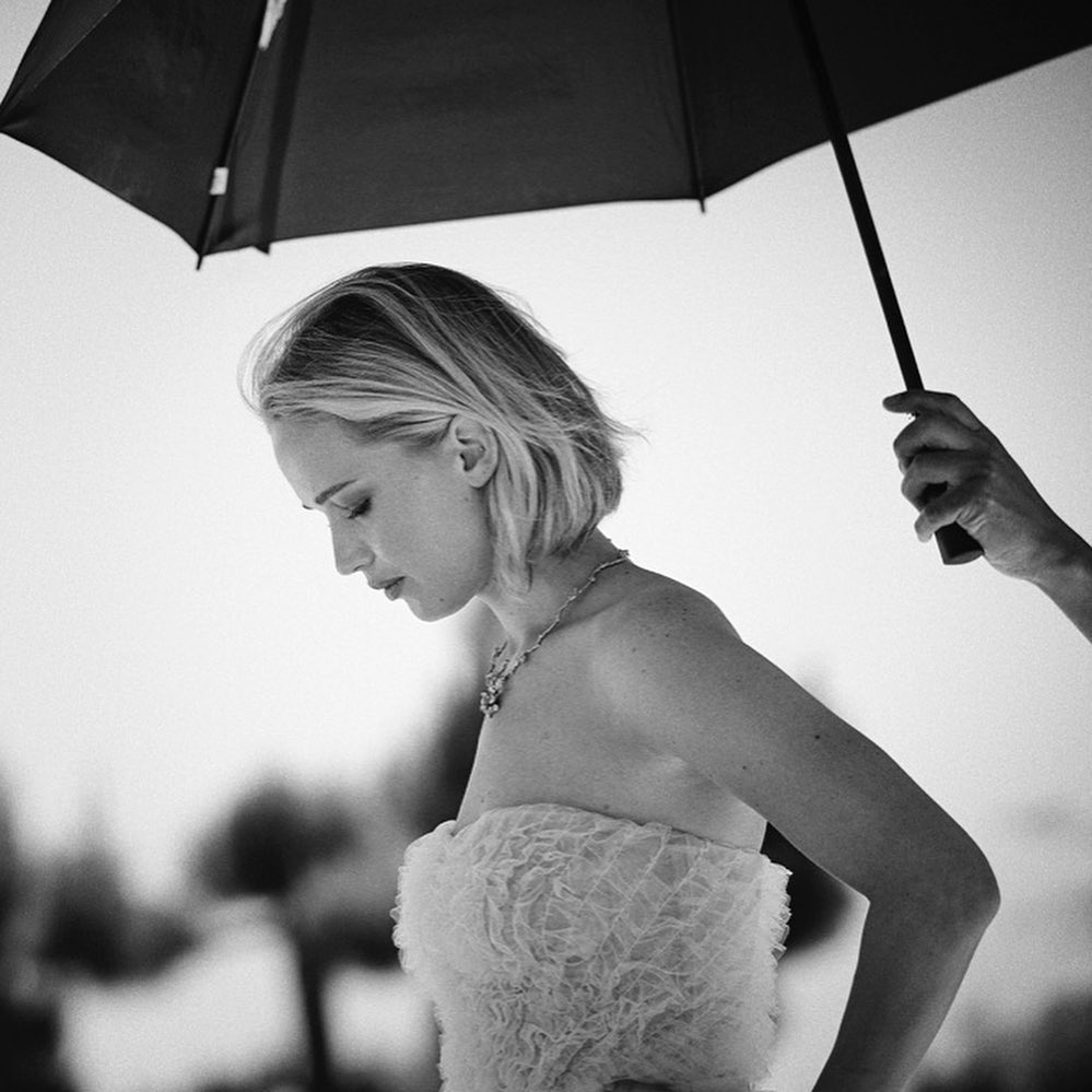 Elegant woman in ruffled strapless dress with diamond necklace, posed under an umbrella, close-up black and white portrait. 
