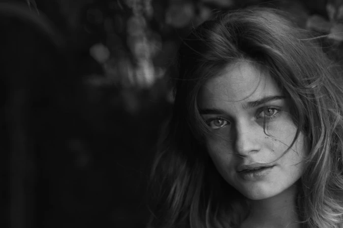 Close-up monochrome portrait of a young woman with tousled hair looking directly at the camera.
