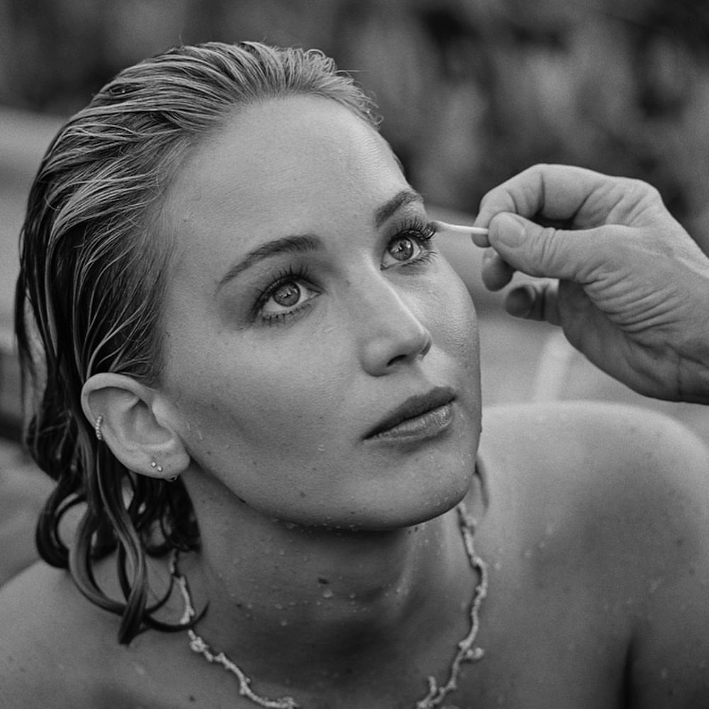 Black and white portrait of Jennifer Lawrence receiving makeup touch-ups, featuring a close-up shot of her face and wet hair.