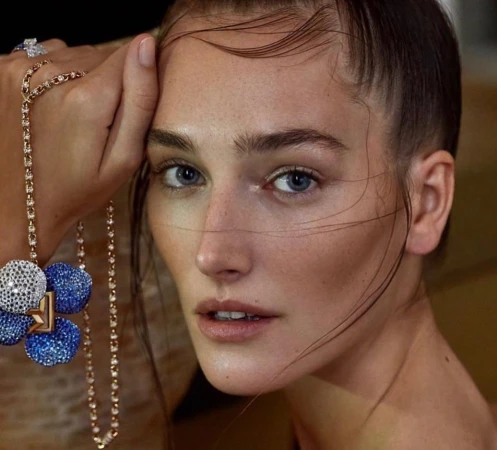 Close-up portrait of a woman with wet styled hair holding a diamond and blue sapphire floral necklace to her face.