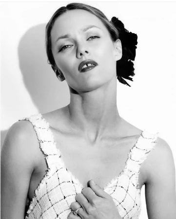 Black and white portrait of a woman wearing a tweed top and a dark floral hair accessory against a plain white background.