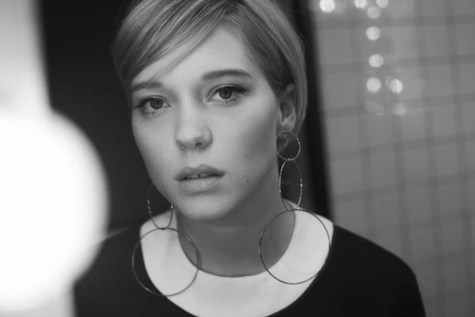Close-up portrait of a woman with short blonde hair wearing large hoop earrings and a dark top by photographer Eric Guillemain.