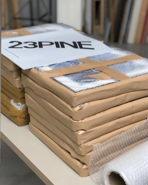 Stacked wrapped art pieces on a white surface, featuring a sign with '23PINE' in bold black text, bubble wrap, and cardboard.