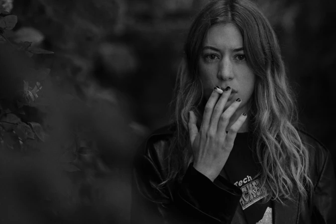 Black and white portrait of a woman smoking a cigarette outdoors, wearing a dark leather jacket.