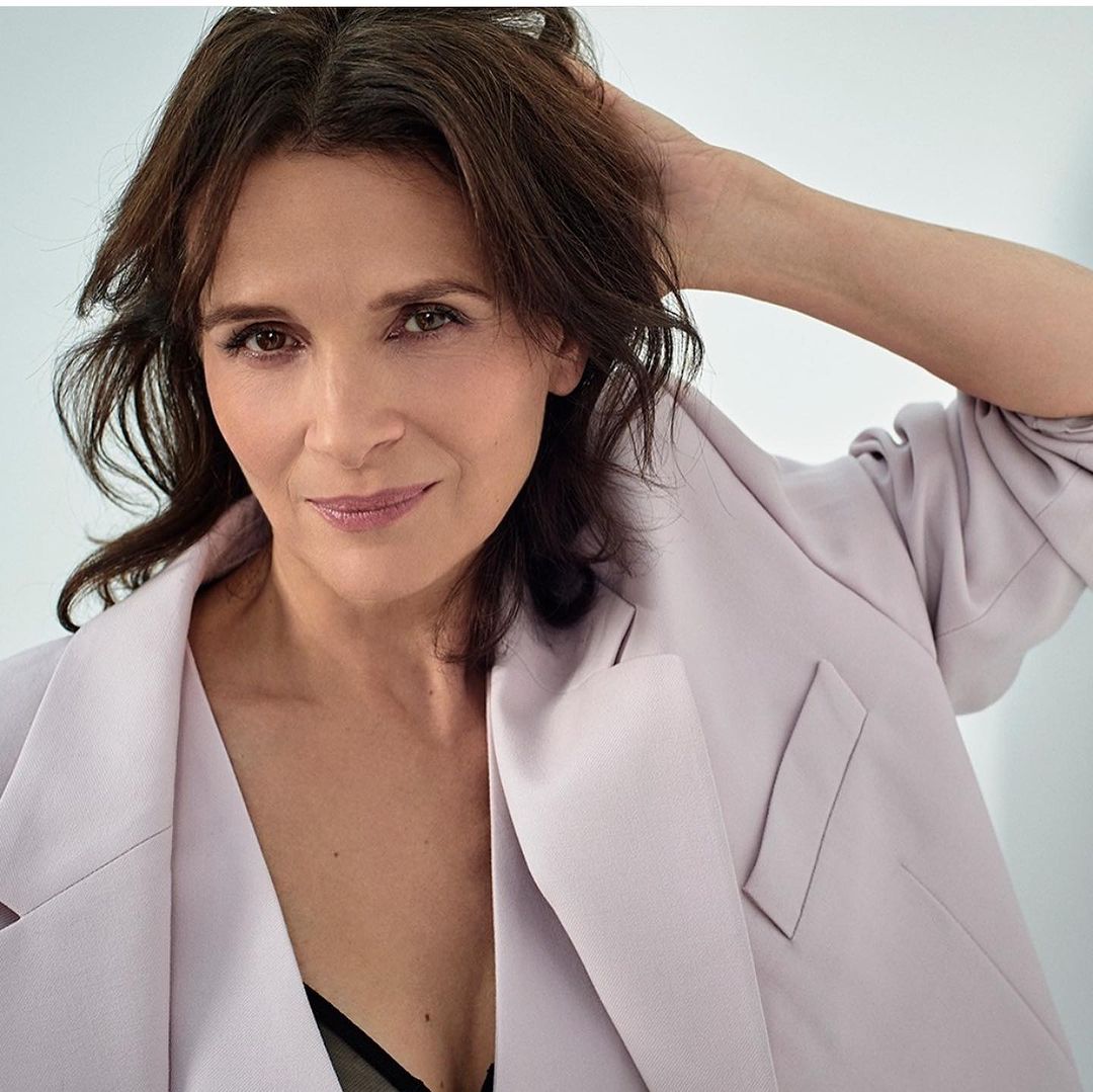 Elegant woman in a lilac blazer strikes a pose, hand gracefully placed behind her head, complemented by her dark hair and soft makeup.