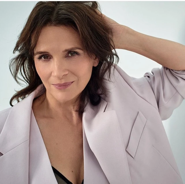 Elegant woman in a lilac blazer strikes a pose, hand gracefully placed behind her head, complemented by her dark hair and soft makeup.