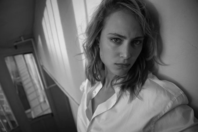 Monochrome portrait of a woman leaning against a wall wearing a white button-down shirt by photographer Eric Guillemain.