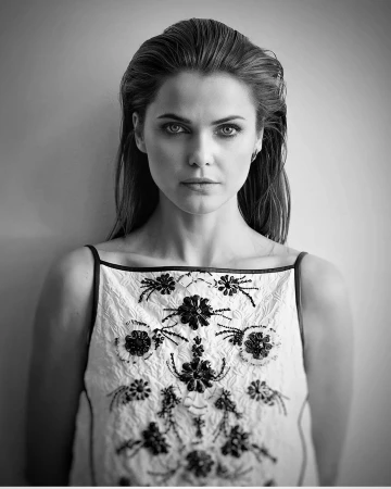 Portrait of a woman with slicked-back hair wearing an embroidered white top against a neutral background.