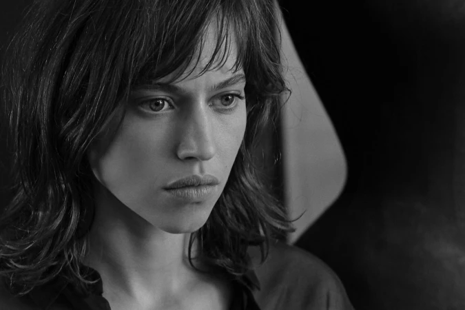 Close-up black and white portrait of a woman with dark hair and bangs looking off to the side with a serious expression.