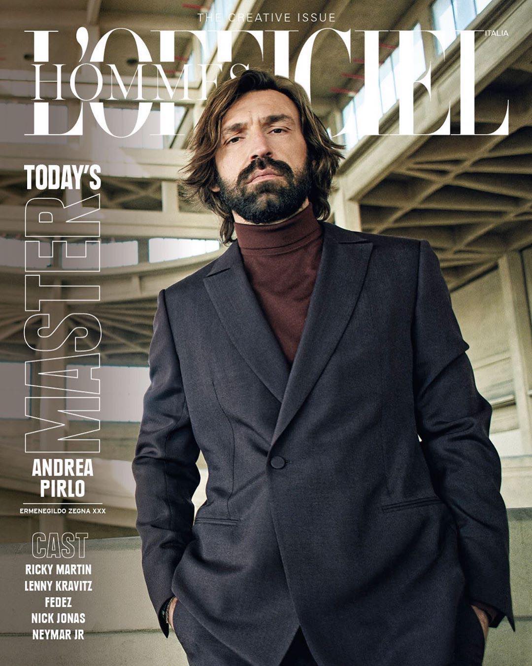 Andrea Pirlo on L'Uomo Vogue magazine cover. He's indoors, wearing a suit jacket and turtleneck. Neutral color palette, architectural background.