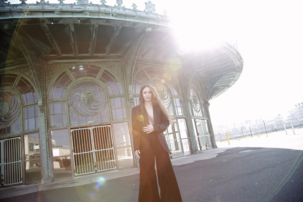 Woman in a dark suit standing outside an ornate curved pavilion with sun flare overhead