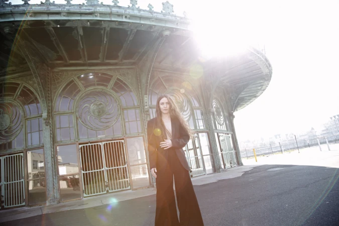 Woman in a dark suit standing outside an ornate curved pavilion with sun flare overhead