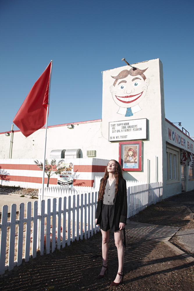 Woman posing outdoors by the Wonder Bar building under a clear blue sky, featuring vintage signage and red and white striped decor.