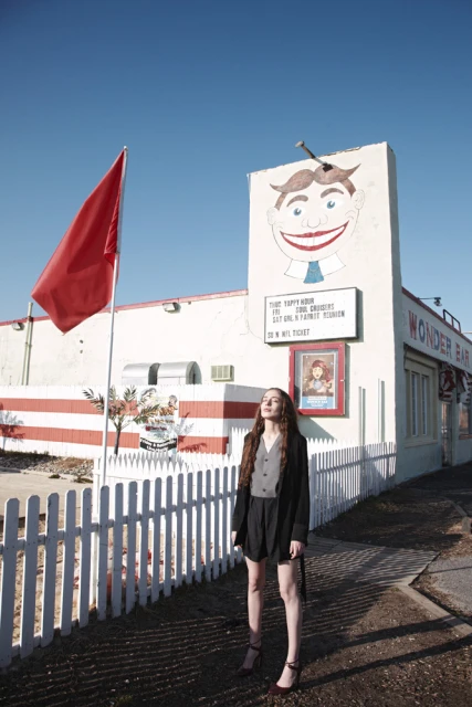 Woman posing outdoors by the Wonder Bar building under a clear blue sky, featuring vintage signage and red and white striped decor.