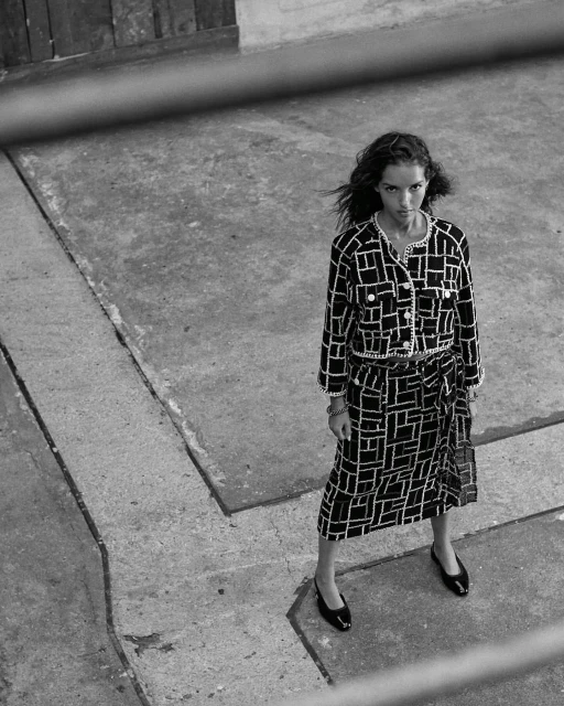 Woman in a black and white patterned two-piece outfit stands on a concrete surface in a fashion editorial style photograph.